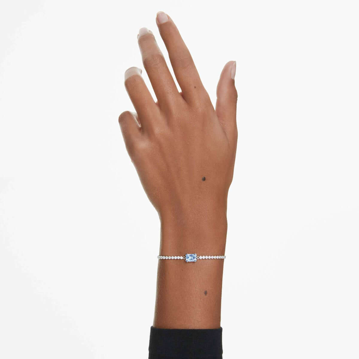 Elegant wrist wearing a delicate Swarovski bracelet with a blue crystal centerpiece, showcasing minimalist jewelry design.