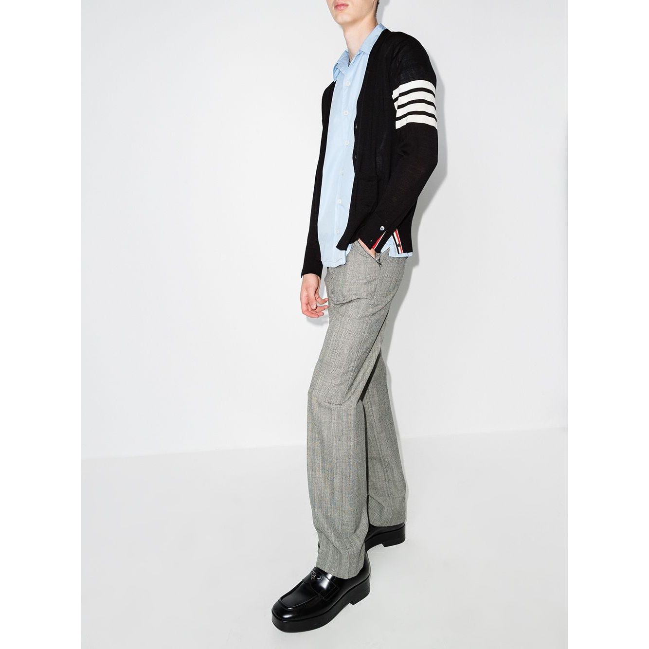 Model wearing Thom Browne Sweaters Blue, navy wool cardigan with 4-Bar stripe and button fastening, paired with grey pants and black shoes.
