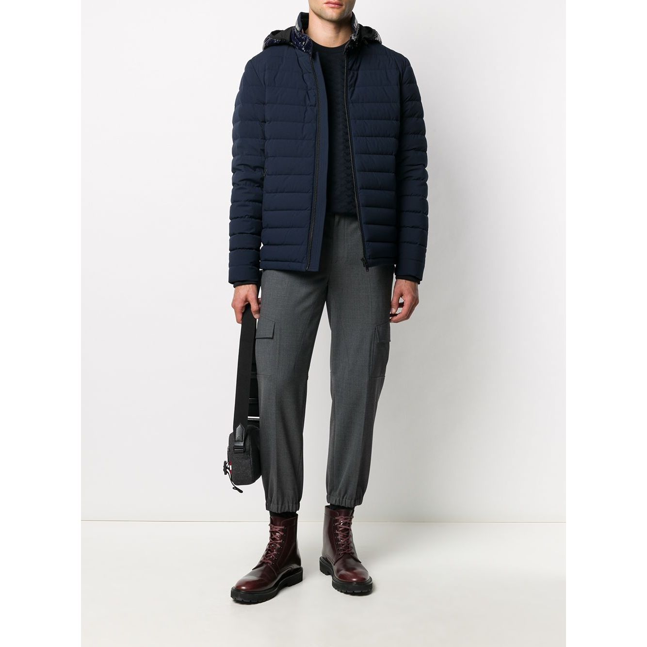 Model wearing navy quilted jacket, grey pants, and brown boots with black shoulder bag
