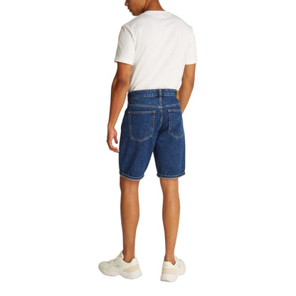 Back view of a model wearing Calvin Klein Jeans Blue Cotton Bermuda Shorts with white sneakers and a white t-shirt.