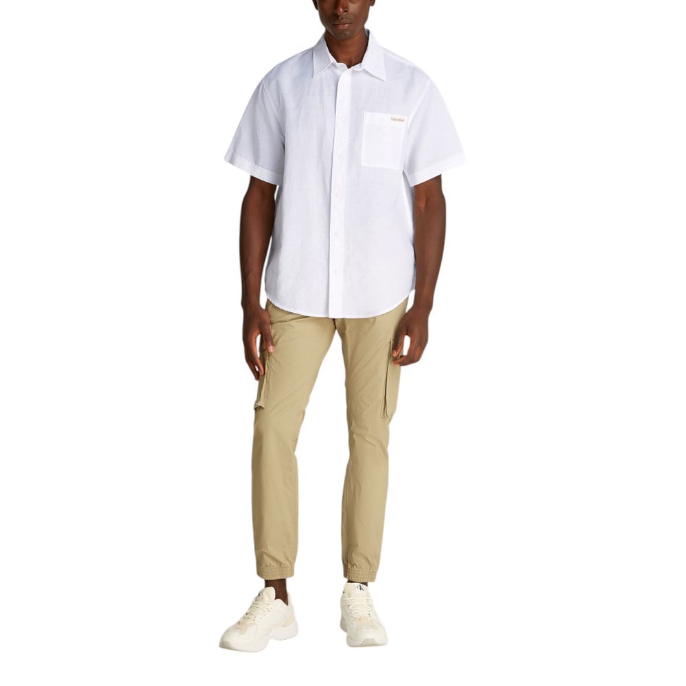 Man wearing Calvin Klein Jeans White Linen Shortsleeve Shirt with beige pants, showcasing summer style and comfort.