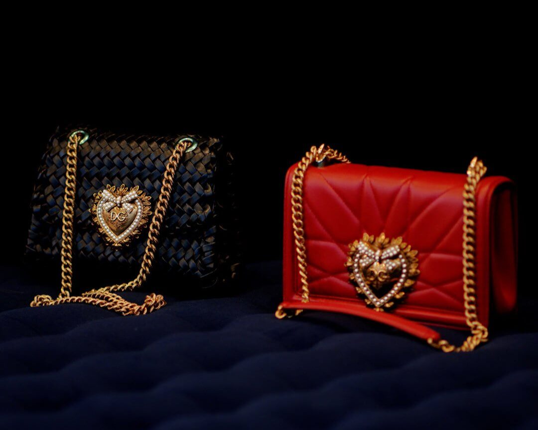 Black and red luxury handbags with gold chain straps and intricate heart-shaped embellishments on a dark and elegant background.