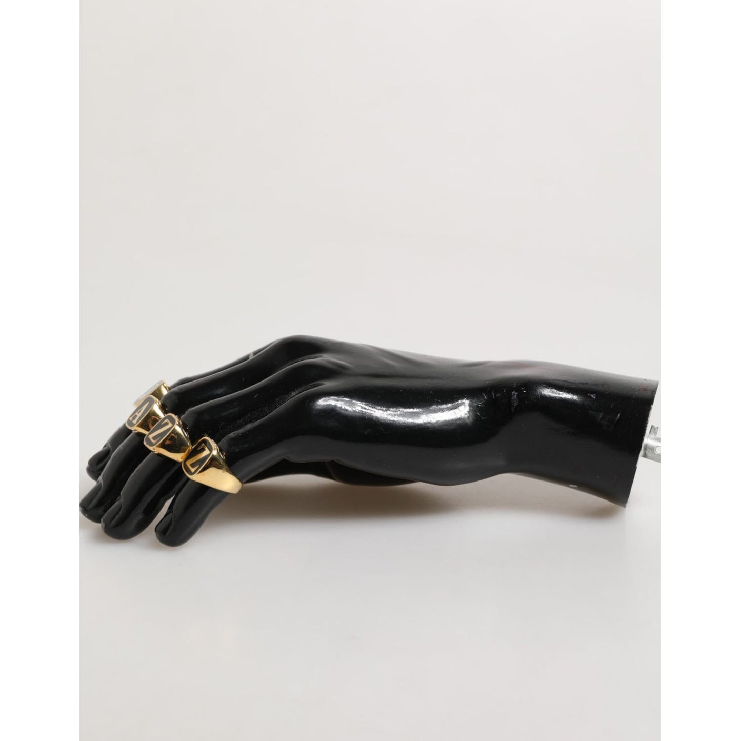 Model wearing Dolce & Gabbana Gold Tone Brass JAZZ Letter Set 4 Pieces Adjustable Ring on black glossy hand for luxury fashion display.