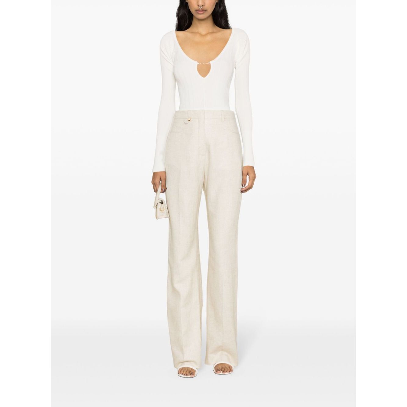 Woman wearing JACQUEMUS Top White with ribbed knit and cut-out detailing, paired with beige trousers and holding a small bag.