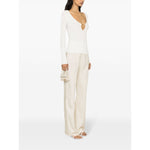 Model wearing JACQUEMUS Top White, a long-sleeve off-white ribbed knit with V-neck and gold-tone logo, styled with wide-leg pants.