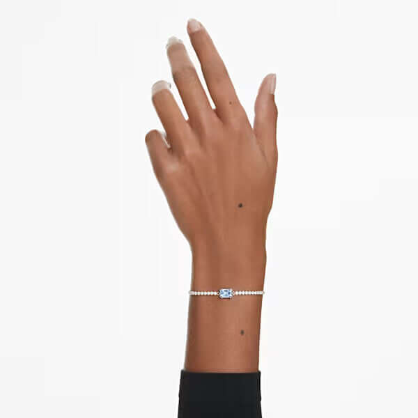 Elegant model showcasing Swarovski bracelet with blue gemstone on wrist against white background.