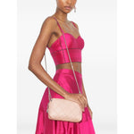 Woman in pink dress holding Tory Burch Fleming leather crossbody bag with diamond quilted design and chain strap.