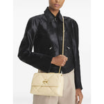 Model holding Tory Burch Kira Diamond small leather shoulder bag in light yellow with gold-tone chain strap and logo plaque.