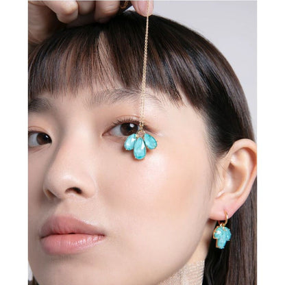 Woman wearing turquoise gemstone earrings and necklace, held above her eye, showcasing elegant jewelry design on a close-up portrait.