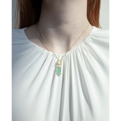 Woman wearing a gold necklace with green pendant against white blouse, showcasing elegant jewelry design.