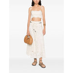 Zimmermann Cropped top with tie-fastening straps and floral detailing paired with matching white lace skirt and woven handbag.